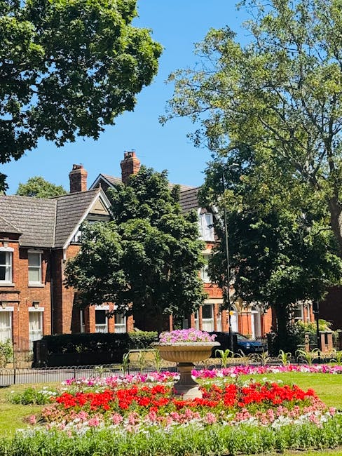 A well-maintained garden featuring a lush, neatly trimmed green lawn bordered by curved flower beds filled with a variety of colorful plants and flowers. In the center, there are large ornamental plan